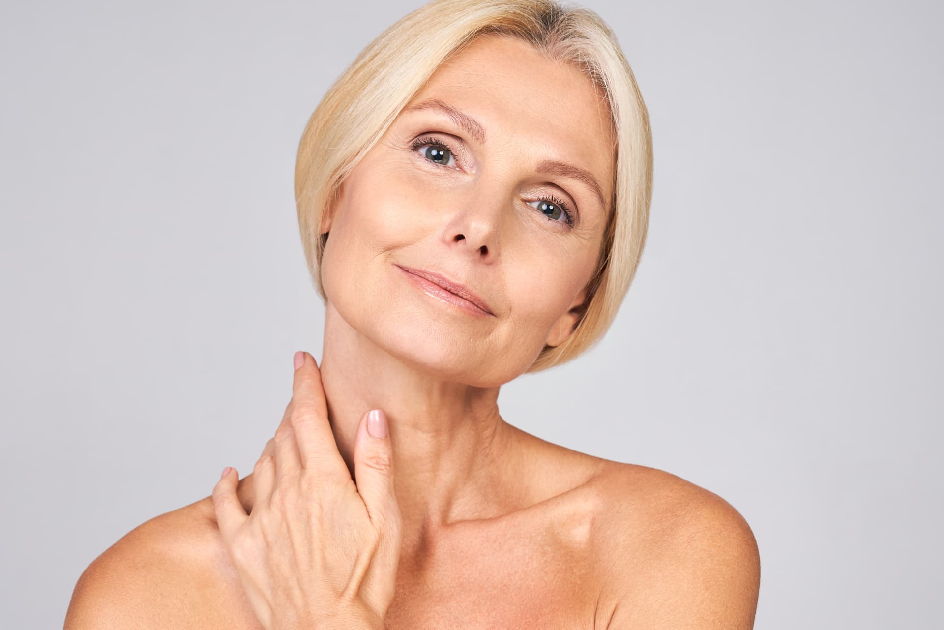 Frau mit Hand am Hals vor grauem Hintergrund